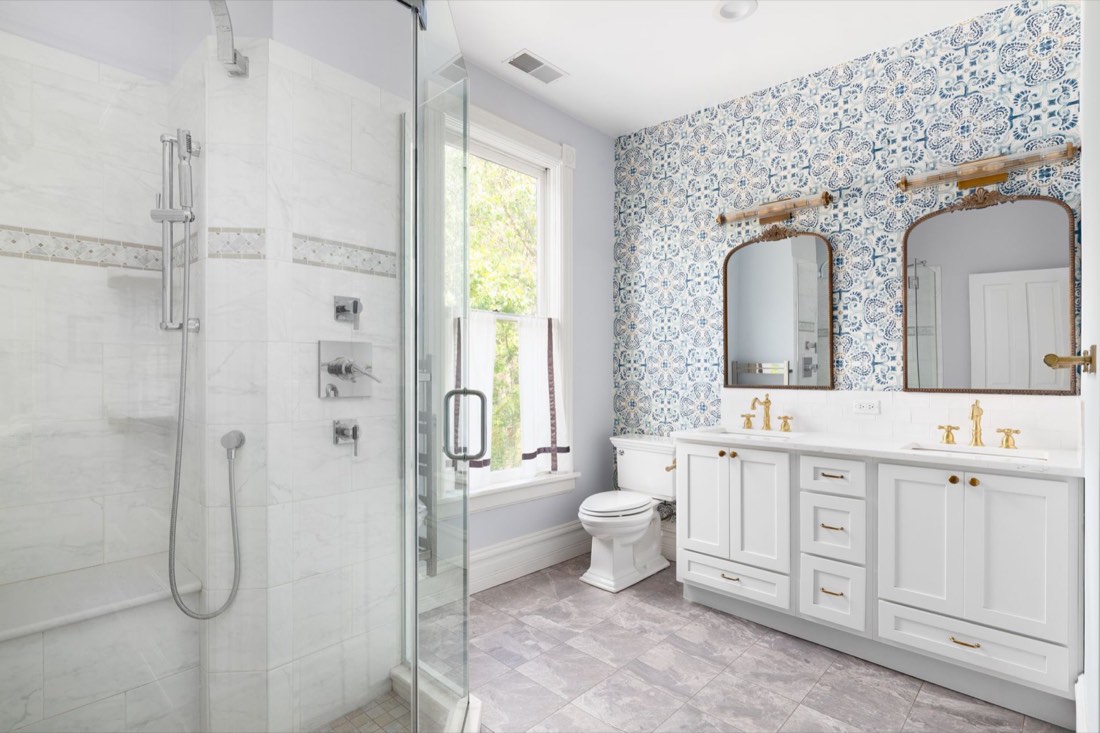 Remodeled bathroom with a glass walk-in shower, patterned wallpaper, and a double vanity