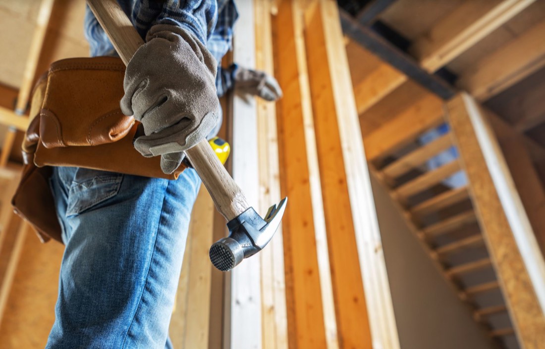 Carpenter with a hammer and tool belt inside a framed addition