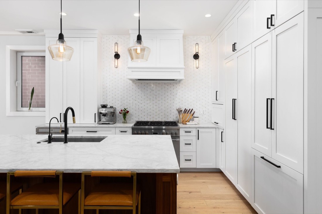 Remodeled white kitchen with a marble island, pendant lights, and hardwood floors