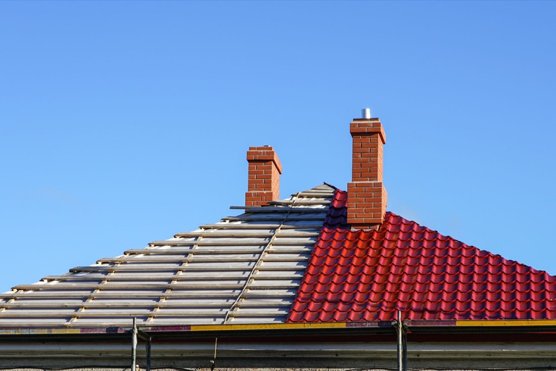 Roof replacement in progress with old tiles removed beside new red tiles and brick chimneys