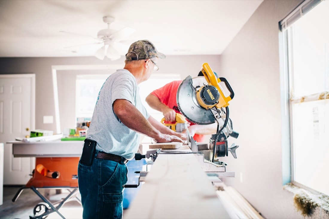 Carpenters cutting trim with a miter saw inside a home under renovation