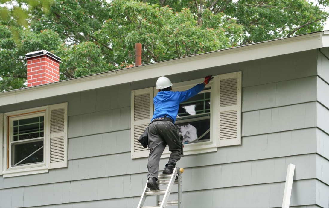 Installer on a ladder fitting a replacement window into a home's siding